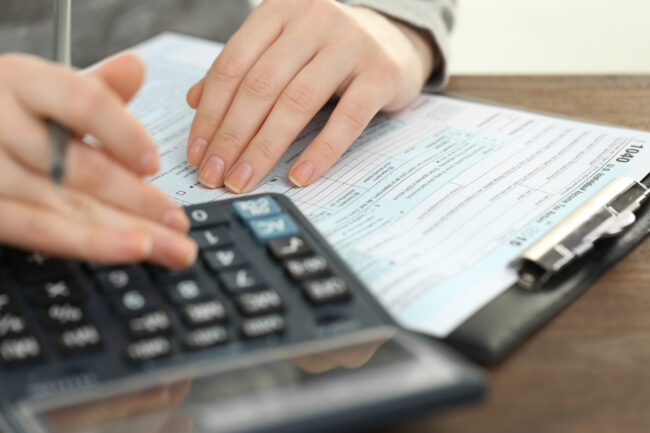 Female,Hand,Holding,A,Pen,And,Using,Calculator,While,Filling