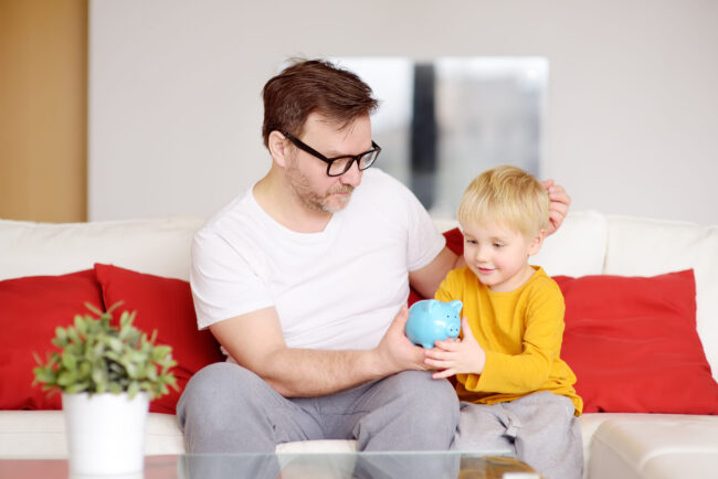 Father,And,Son,Putting,Coin,Into,Piggy,Bank.,Education,Of