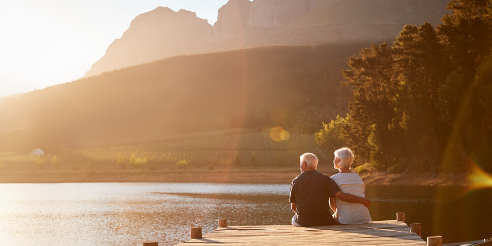 Romantic,Senior,Couple,Sitting,On,Wooden,Jetty,By,Lake