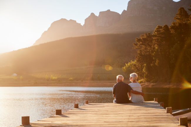 Romantic,Senior,Couple,Sitting,On,Wooden,Jetty,By,Lake